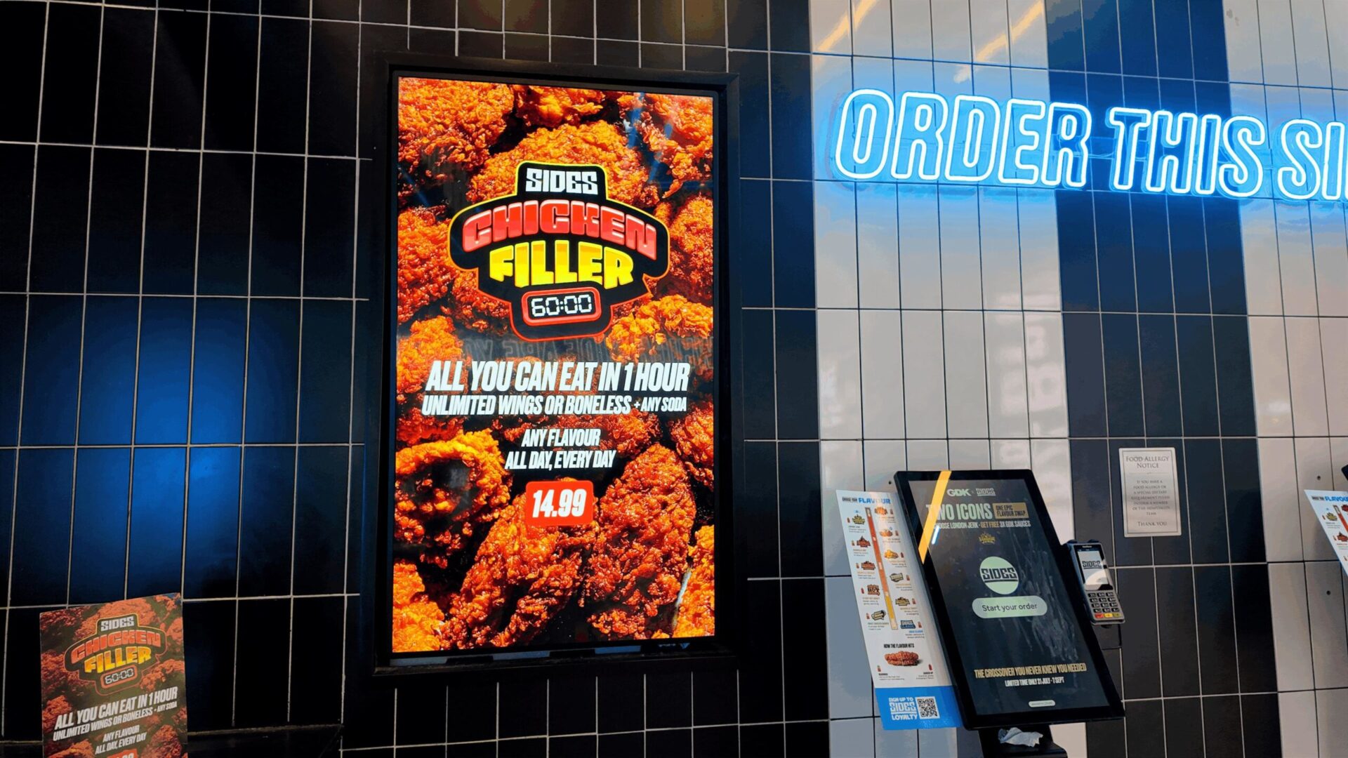 Feeling adventurous? A digital display at Sides promotes its one-hour, all-you-can-eat Chicken Filler offer beside a self-service ordering kiosk. Image: Nowsignage)