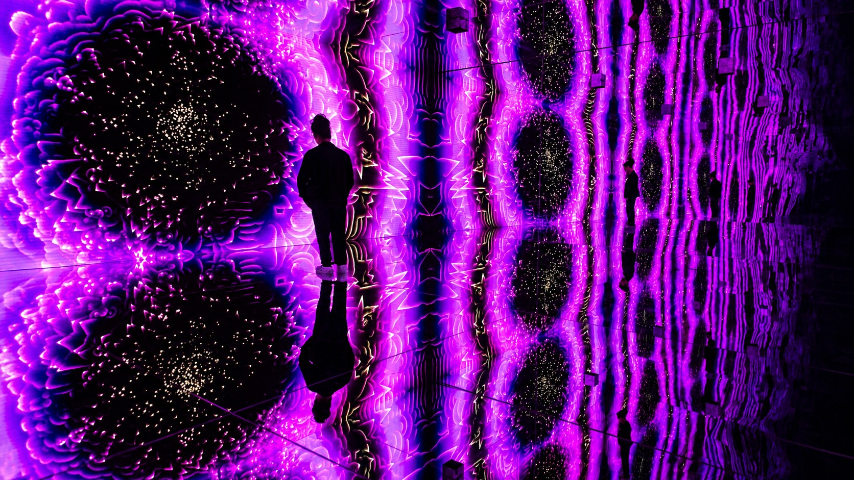 A visitor explores Nubank Arte Lab's infinity room, where mirrored surfaces reflect vivid LED imagery to create the illusion of an endless digital environment (Image: ON)