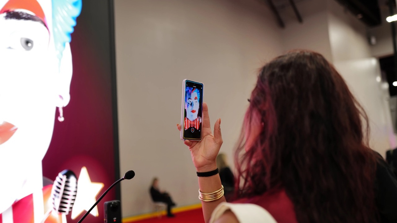 A visitor photographs an AI Host character at IMEX America 2026 in Las Vegas. The installation combined a large LED display, real-time animation and AI-powered conversations. (Image: Newmedia)